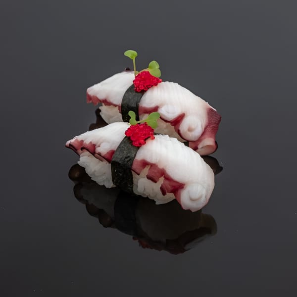 Two pieces of octopus nigiri sushi, garnished with red roe and green sprouts on a dark surface.