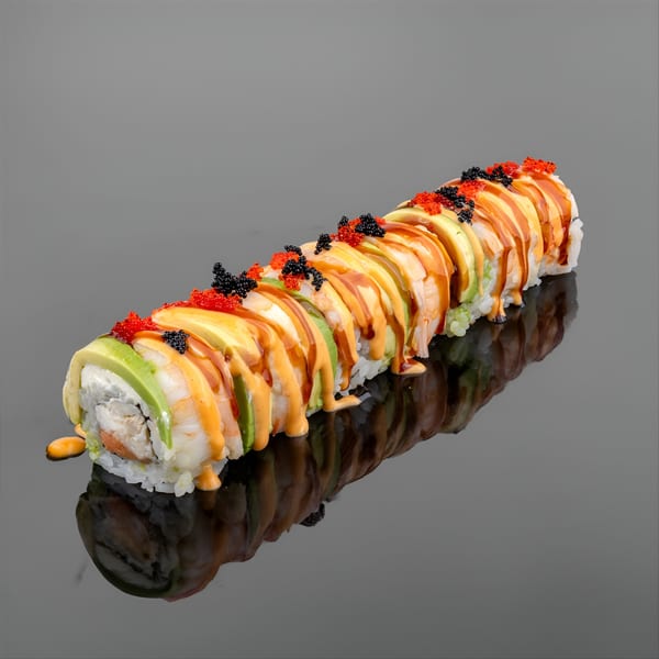 YuGo Sushi & More's sushi roll with avocado, shrimp, sauce, and colorful roe on a dark reflective surface.