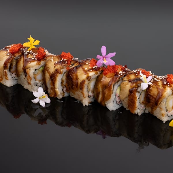 YuGo Sushi & More's Dragon Roll, garnished with colorful flowers and tobiko, on a reflective dark surface.