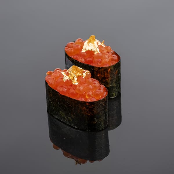 Two gunkan maki sushi pieces topped with bright orange salmon roe and gold flakes.